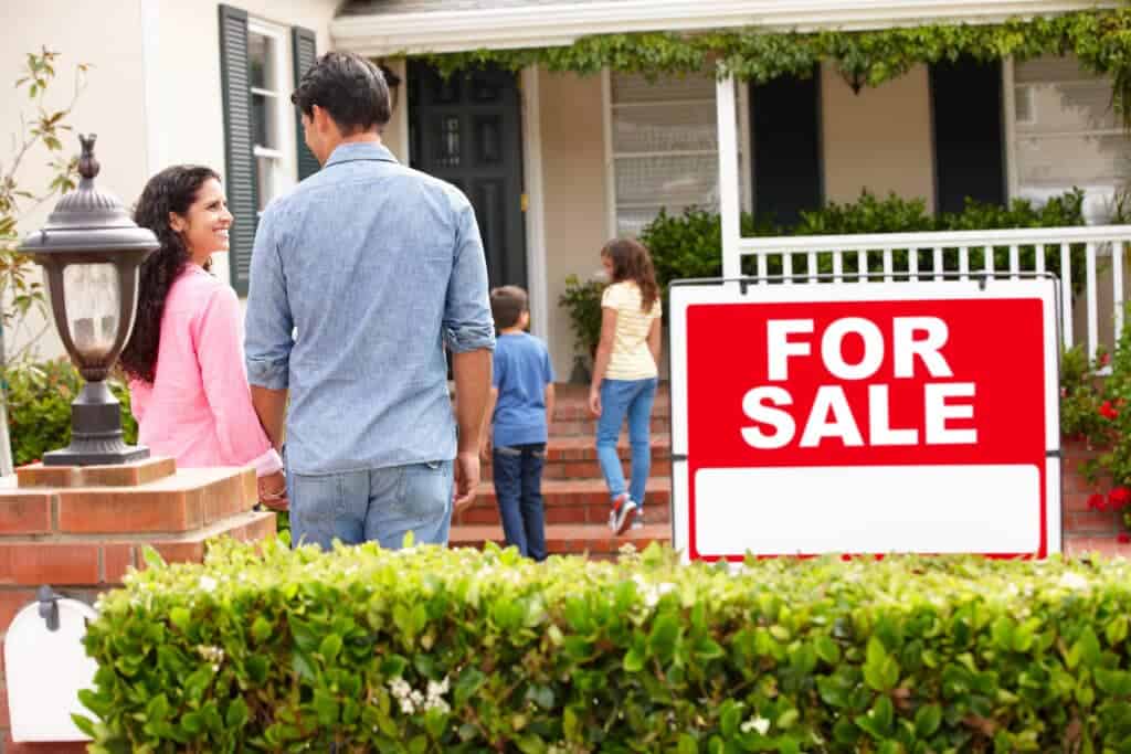 family outside home with for sale sign